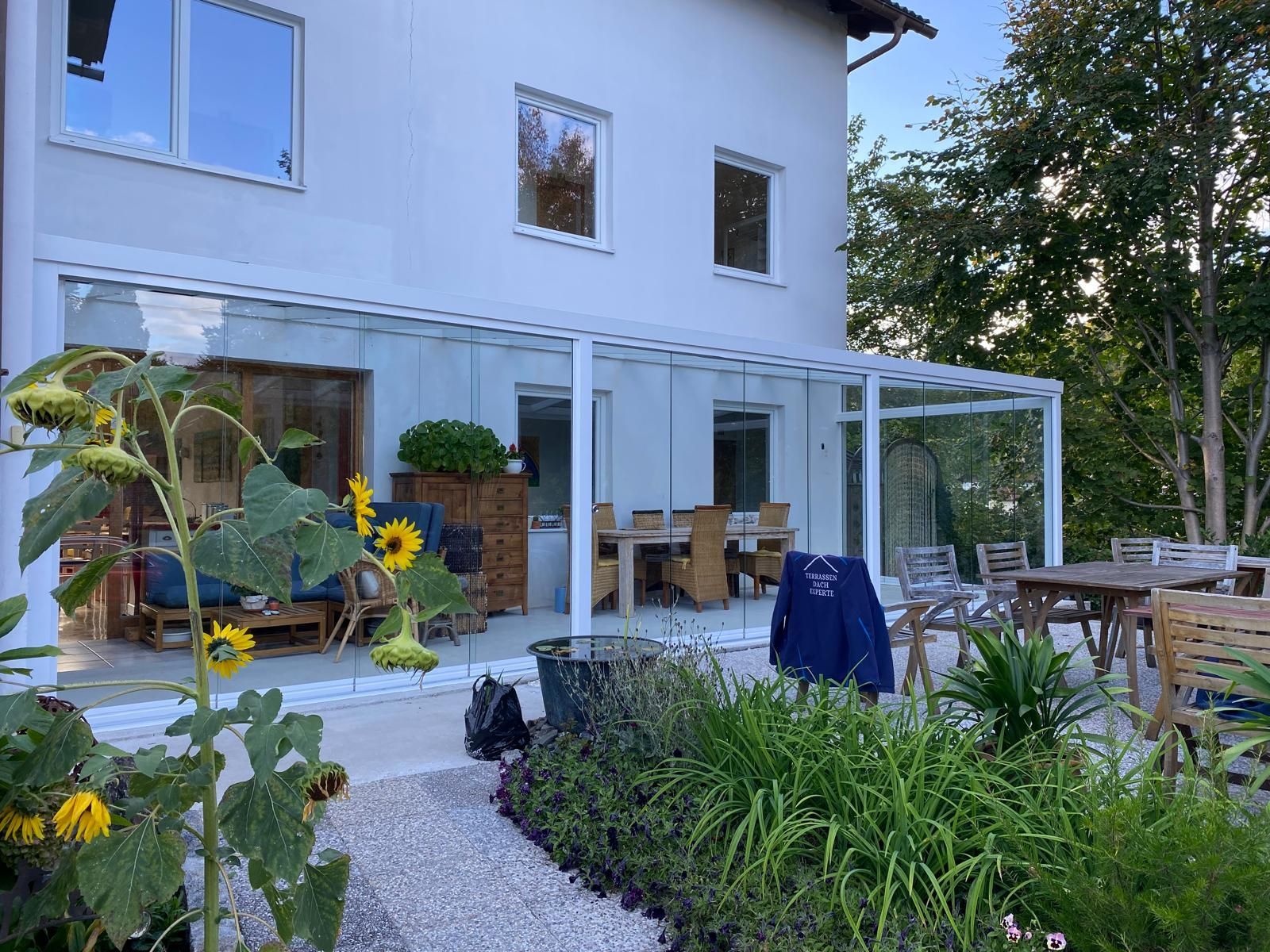 Balkon in der Abenddämmerung mit Blick auf eine Stadt mit Bergkulisse; beleuchteter Tisch und Sitzgelegenheiten.