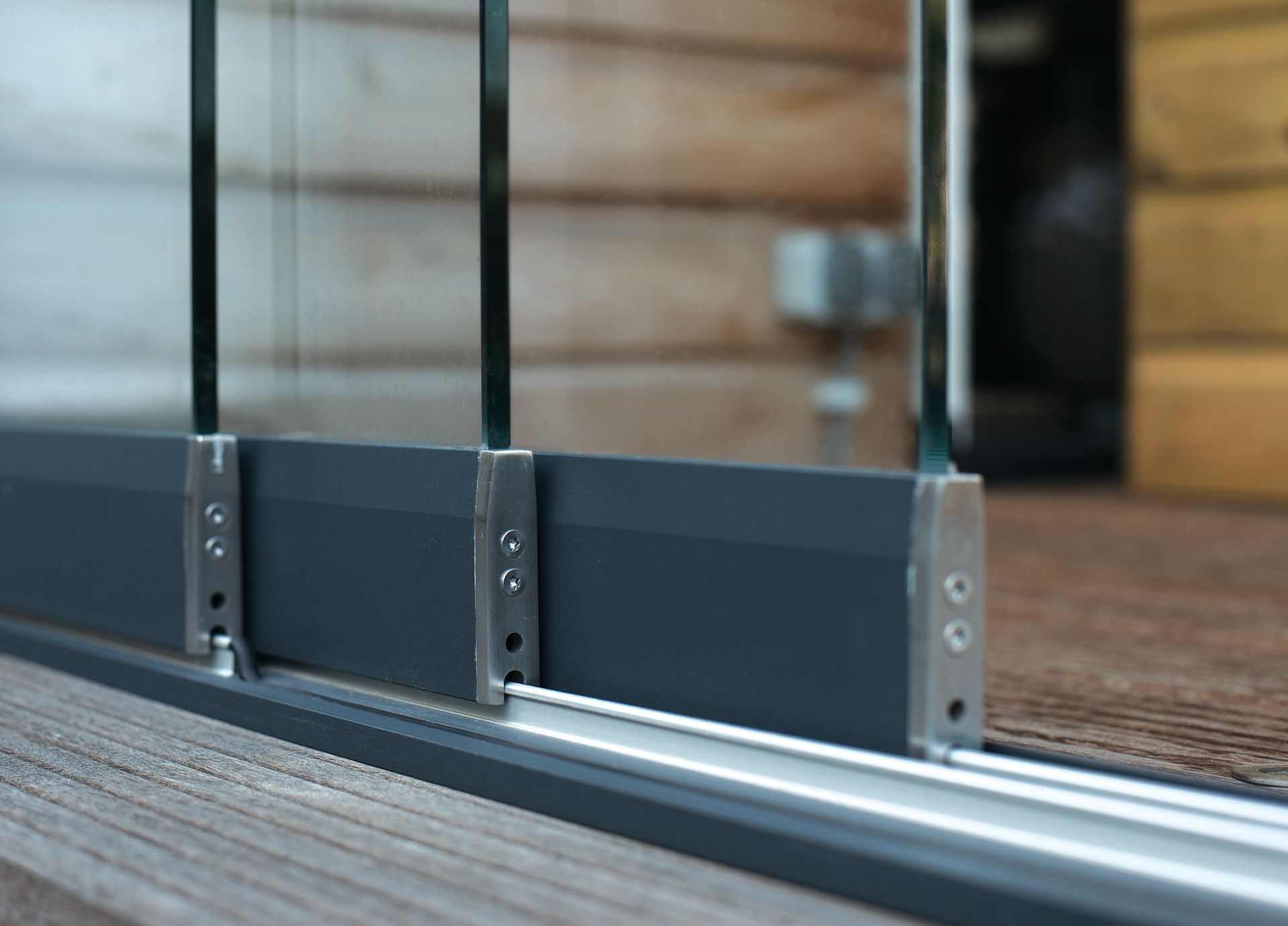 Glasschiebetür mit grauem Rahmen, Metallhalterungen und Holzboden, im Innenbereich.