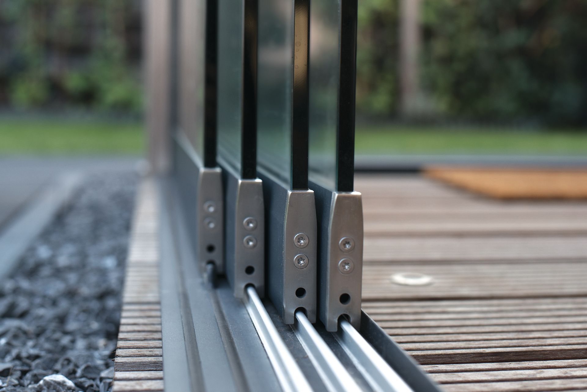 Glasschiebetüren auf einem Holzdeck mit silbernen Beschlägen und Kiesrand.