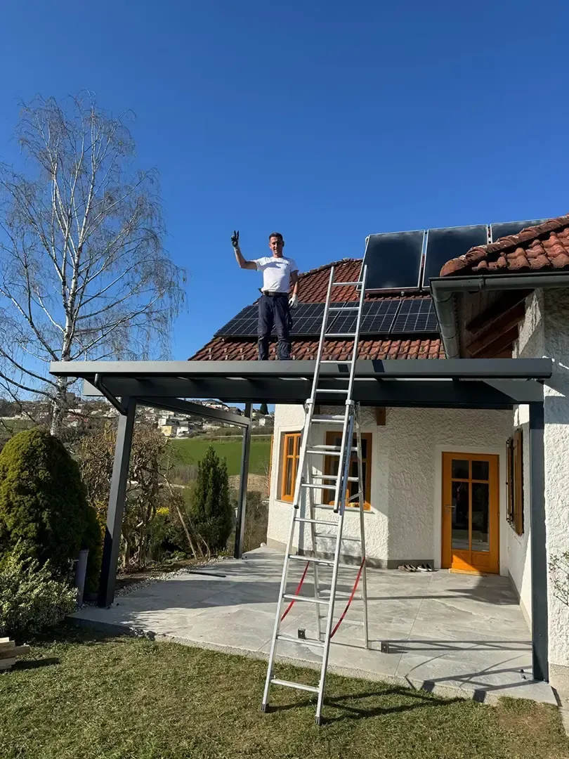 Mann im grauen Arbeitsanzug installiert eine Glasschiebetür in einem im Bau befindlichen Raum.