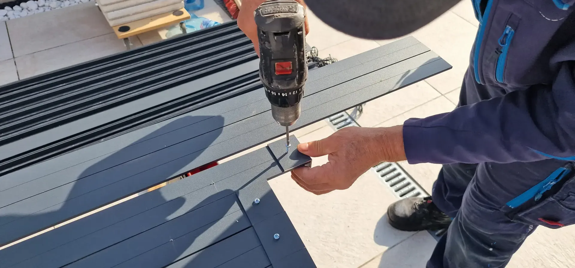 Bauarbeiter bauen eine Terrassenüberdachung auf einem Wohngrundstück mit einem weißen Haus, grünem Gras und einem benachbarten rosa Haus.