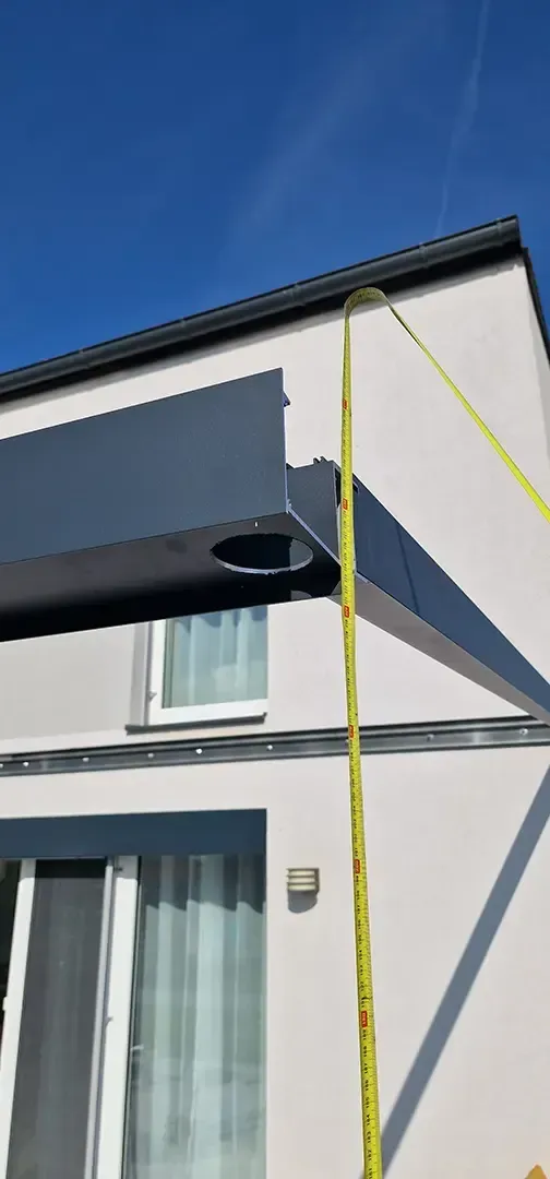 Person in orangefarbener Weste verwendet ein Maßband auf einer braunen Oberfläche.