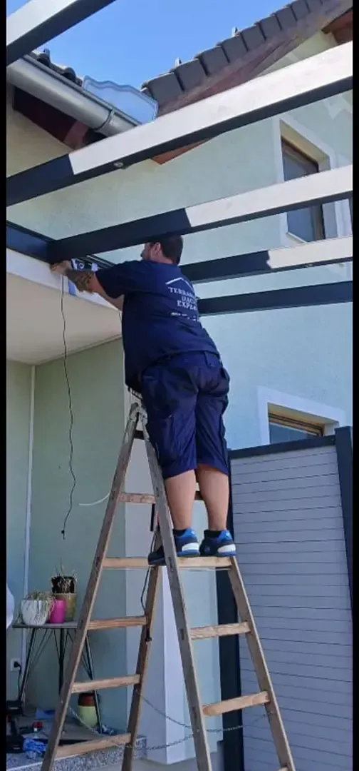 Person, die im Freien eine Holzterrassendiele mit einer Bohrmaschine festschraubt.