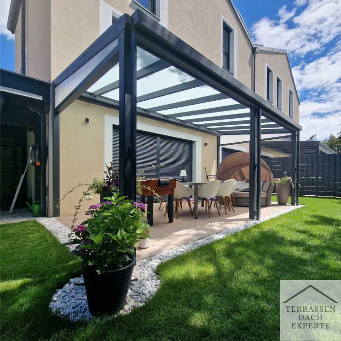 Glass-walled sunroom attached to a green house, lit up at night. White frame, plants in foreground.