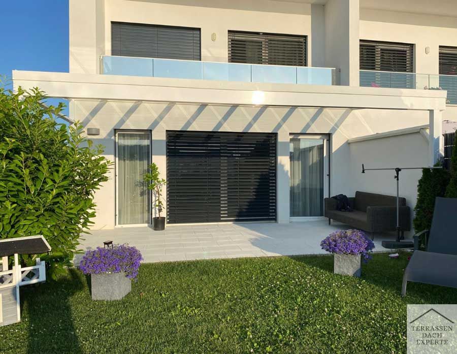 Exterior view of a modern white house with a patio, lawn, and bushes.