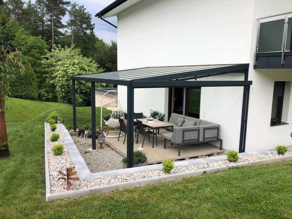 Patio with a pergola, furniture, and landscaping next to a white house with green surroundings.