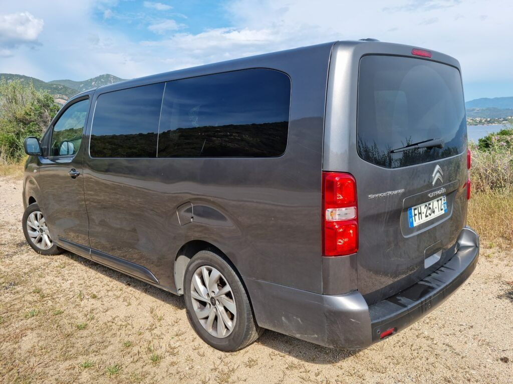 Une camionnette Mercedes grise garée sur un chemin de terre au bord de collines verdoyantes sous un ciel bleu.