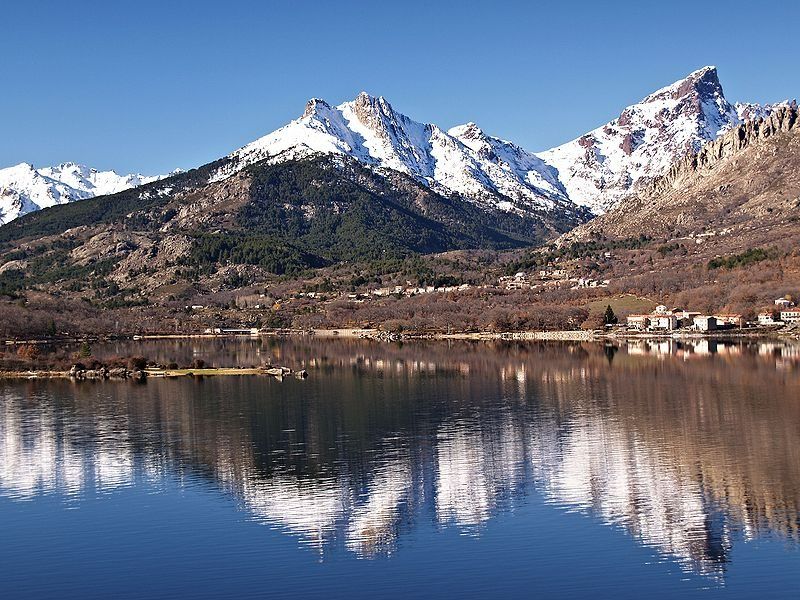 Des sommets enneigés se reflètent dans un lac calme sous un ciel d'un bleu limpide.
