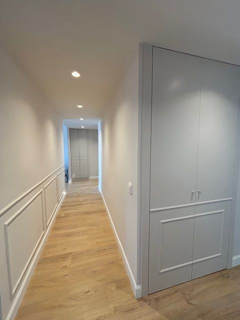 Un largo pasillo con suelos de madera y paredes blancas.