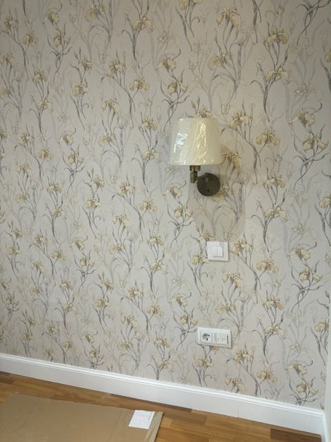Una lámpara está colgada en una pared en una habitación con papel tapiz floral.