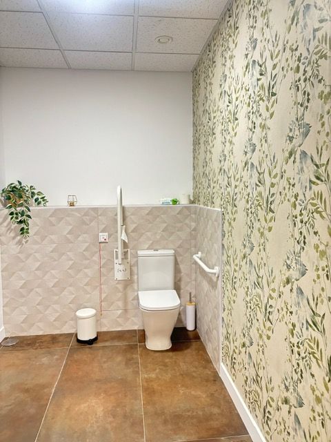 Un baño con inodoro, bote de basura y papel tapiz floral.