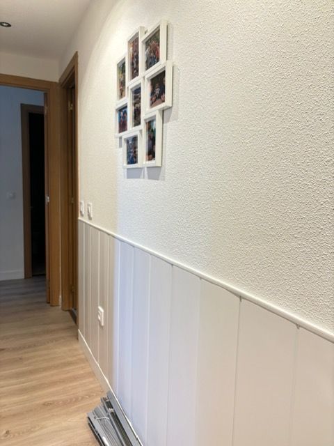 Un pasillo con paredes blancas y suelos de madera y cuadros en la pared.