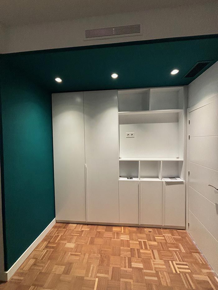 Una habitación con piso de madera, armarios blancos y techo azul.