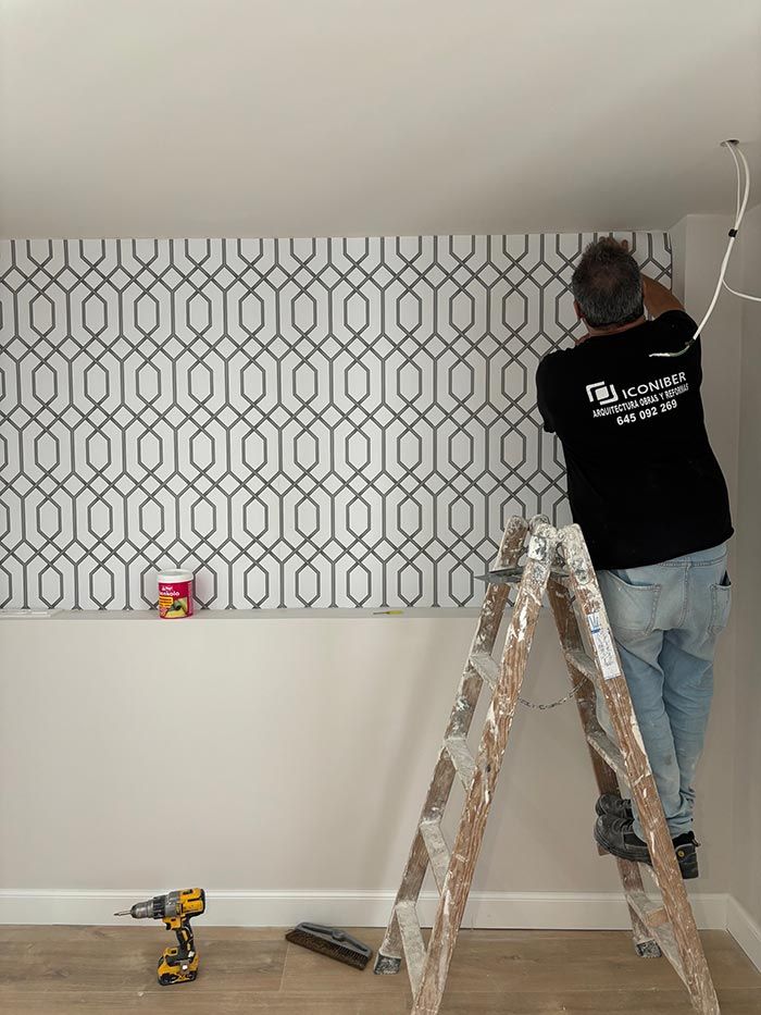 Un hombre está parado en una escalera colgando papel tapiz en una pared.