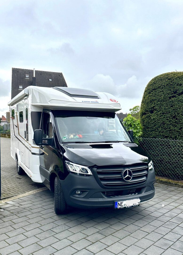 Ein schwarz-weißer Mercedes-Benz Sprinter-Van steht in einer Einfahrt.