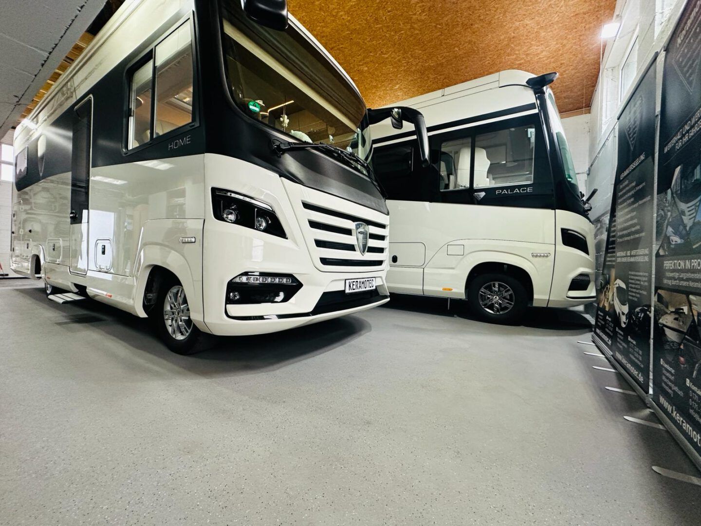 Zwei weiße Wohnmobile stehen nebeneinander in einer Garage.