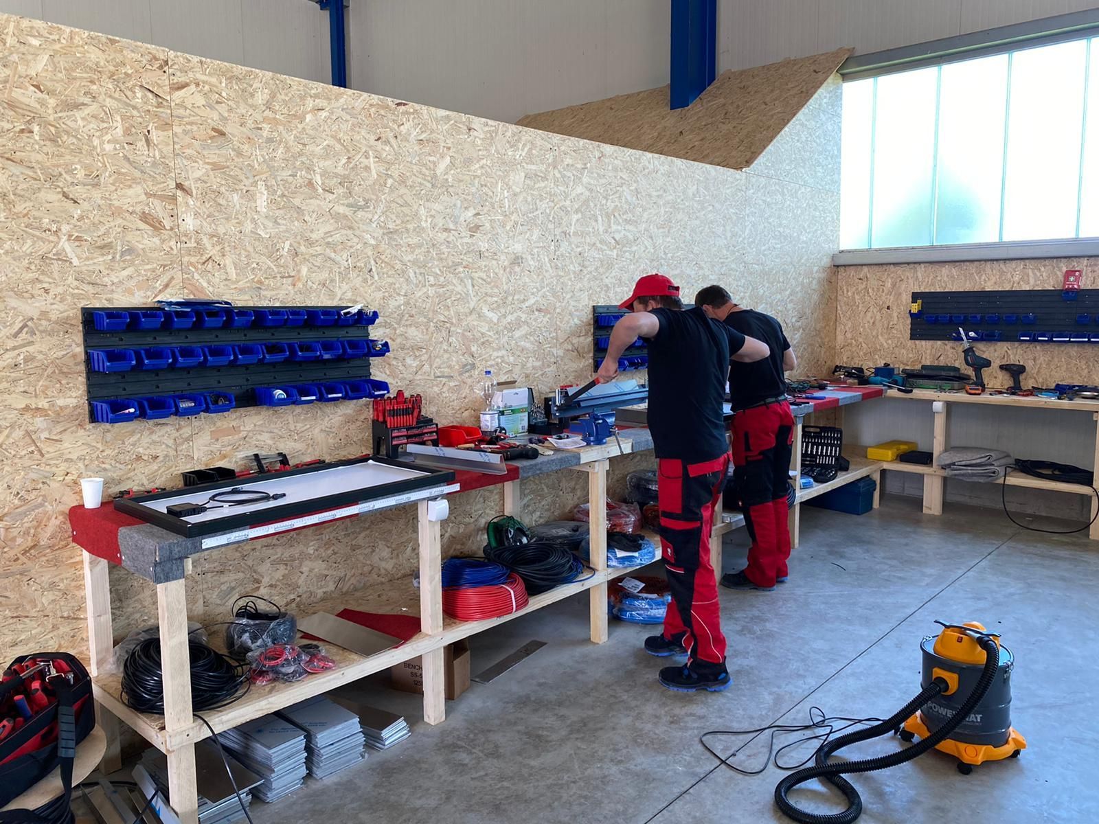 Zwei Männer arbeiten in einer Werkstatt mit einem Staubsauger auf dem Boden.