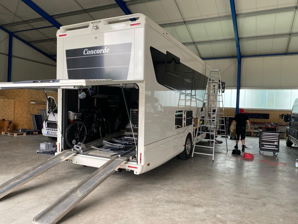 Ein großes weißes Wohnmobil steht in einer Garage und die Hintertür ist offen.