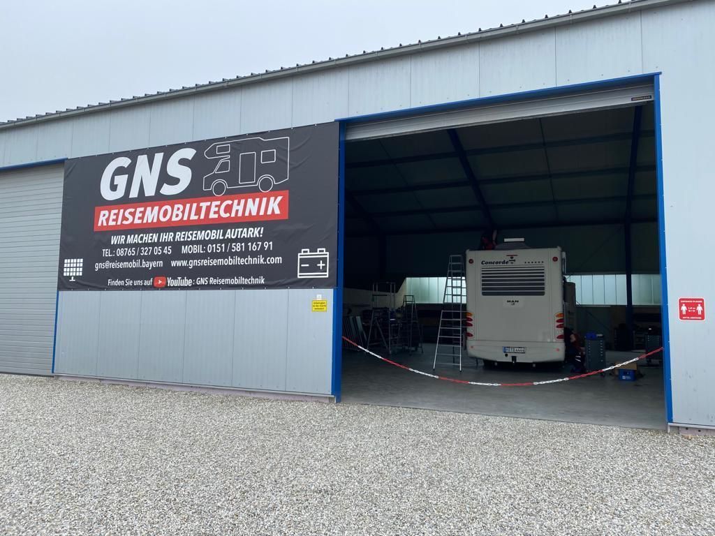 Vor einem gebäude mit einem schild mit der aufschrift „gns reisemobiltechnik“ steht ein wohnmobil.
