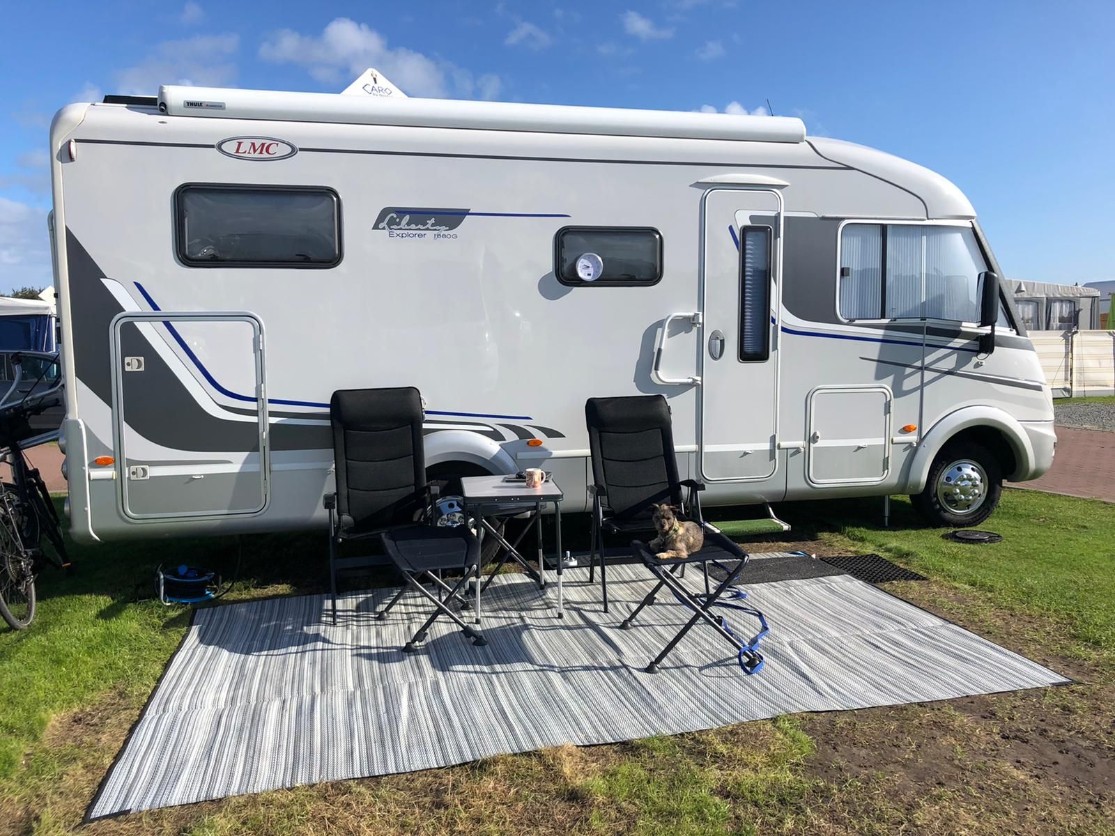 Ein weißes Wohnmobil ist mit Stühlen und einem Tisch auf einer Wiese geparkt.