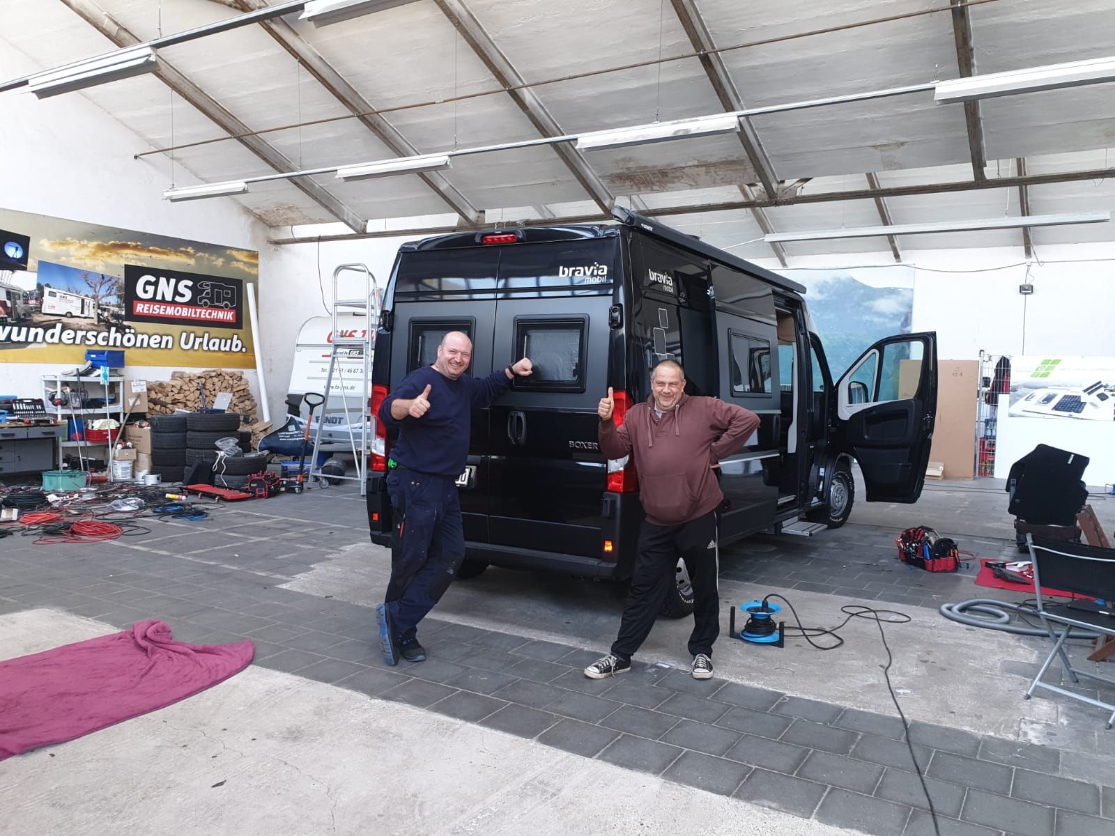 Zwei Männer stehen vor einem Lieferwagen in einer Garage.