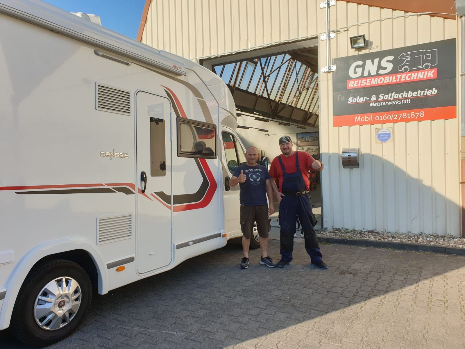 Zwei Männer stehen neben einem weißen Wohnmobil vor einem Gebäude.