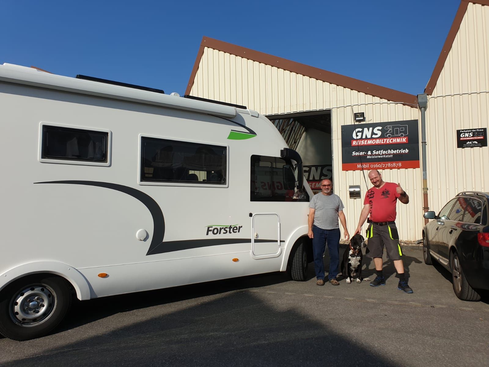 Zwei Männer stehen neben einem weißen Wohnmobil vor einem Gebäude.