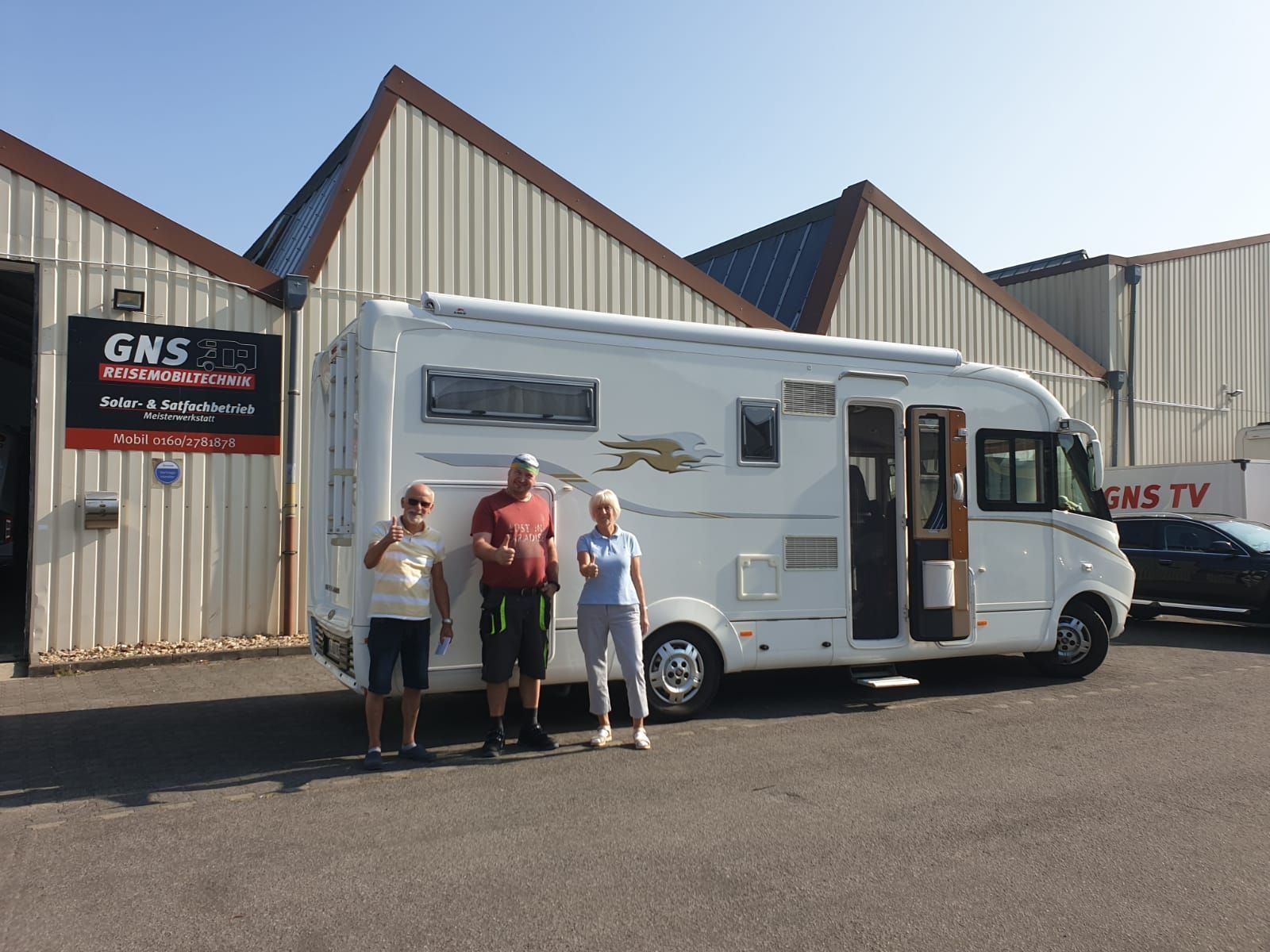 Eine Gruppe von Leuten steht auf einem Parkplatz vor einem Wohnmobil.