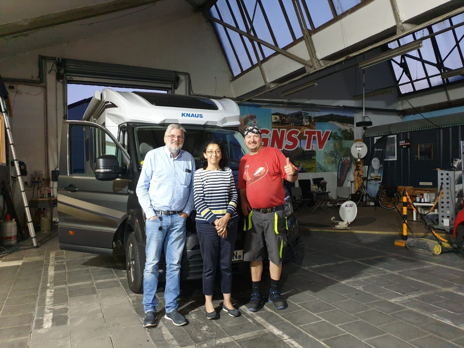 Drei Personen stehen vor einem Wohnmobil in einer Garage.