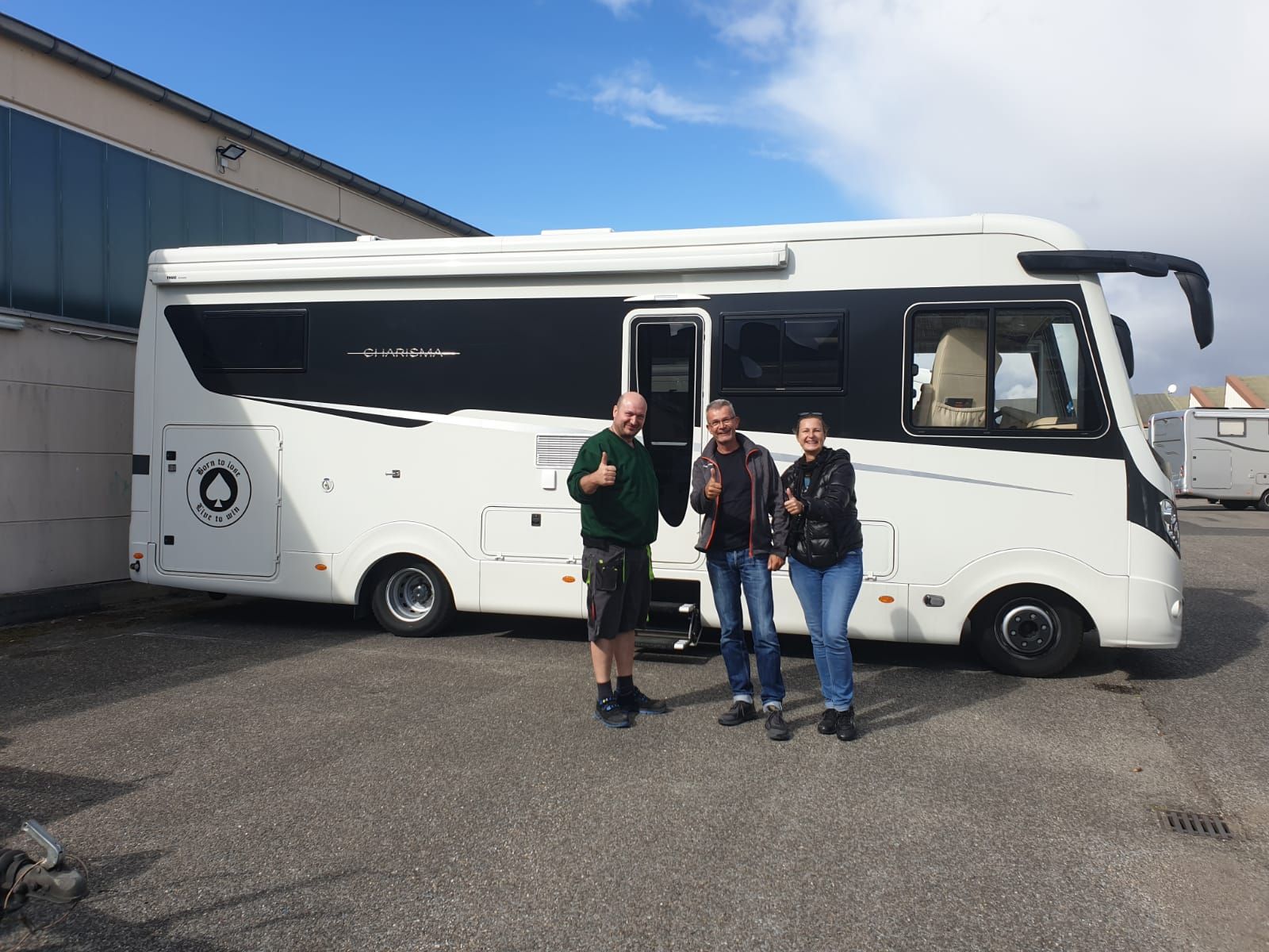 Drei Personen stehen vor einem großen weißen Wohnmobil.