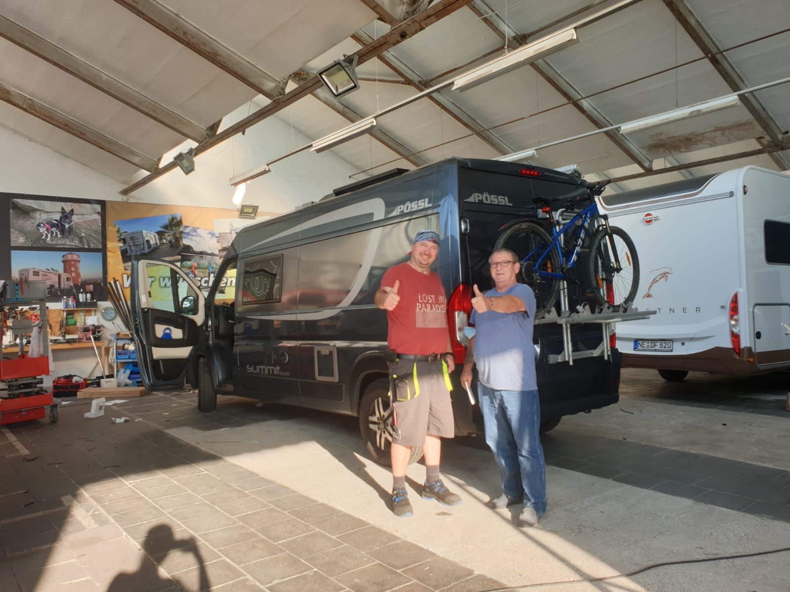 Zwei Männer stehen vor einem Lieferwagen in einer Garage.