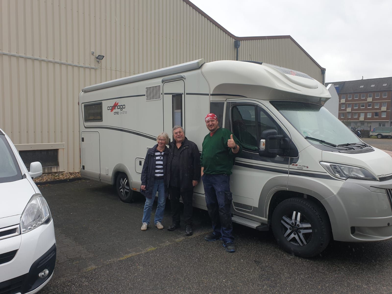 Drei Männer stehen auf einem Parkplatz vor einem Wohnmobil.