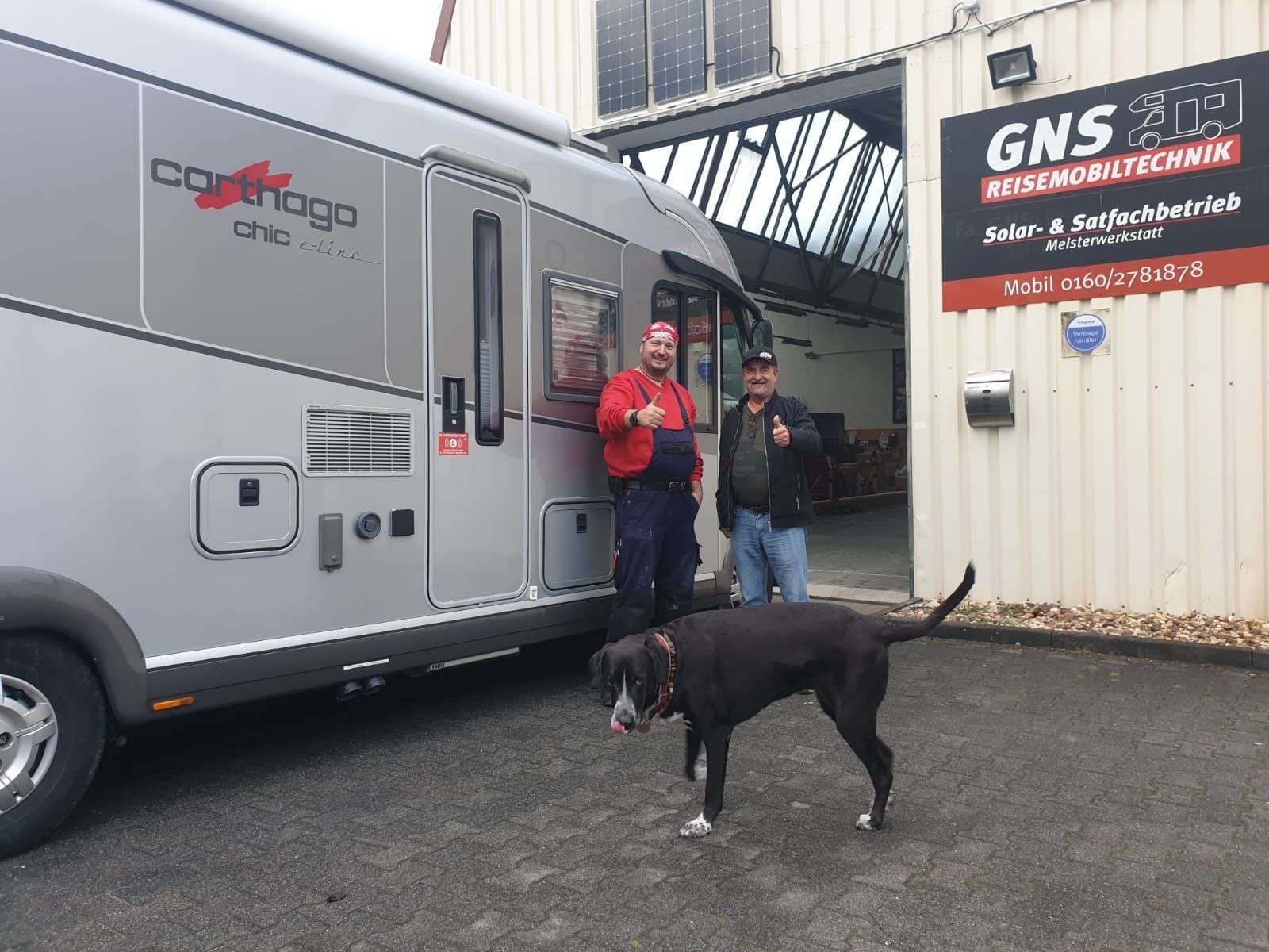Zwei Männer und ein Hund stehen vor einem Wohnmobil.