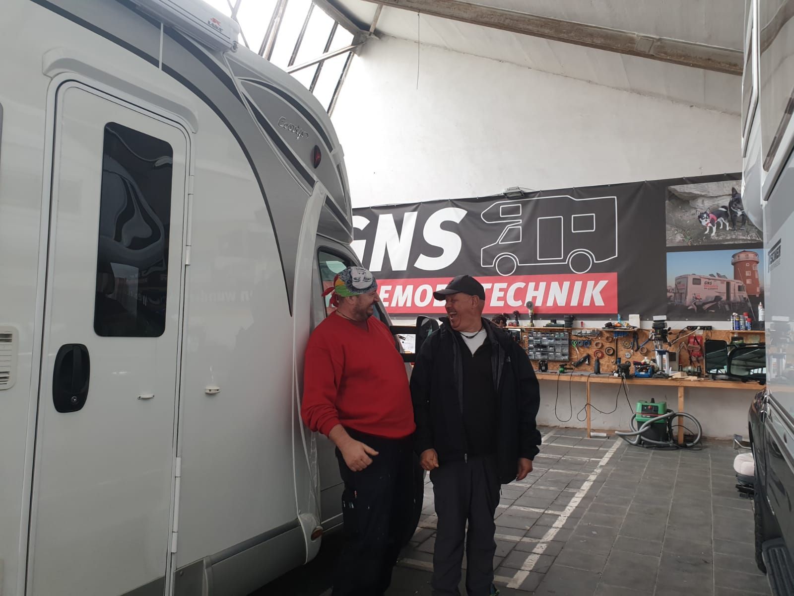 Zwei Männer stehen vor einem Schild mit der Aufschrift „Ens“