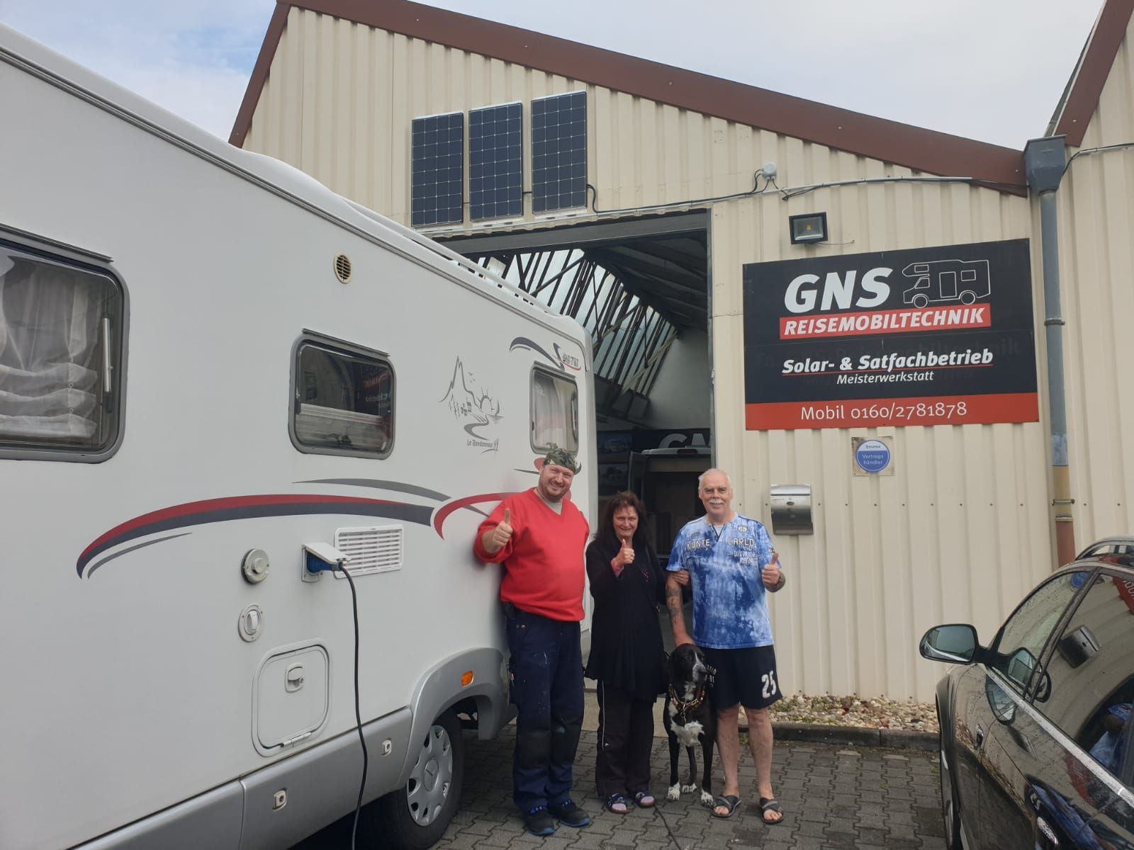 Eine Gruppe von Menschen steht vor einem Gebäude neben einem Wohnmobil.