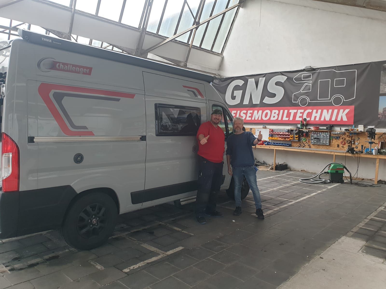 Zwei Männer stehen neben einem weißen Lieferwagen in einer Garage.