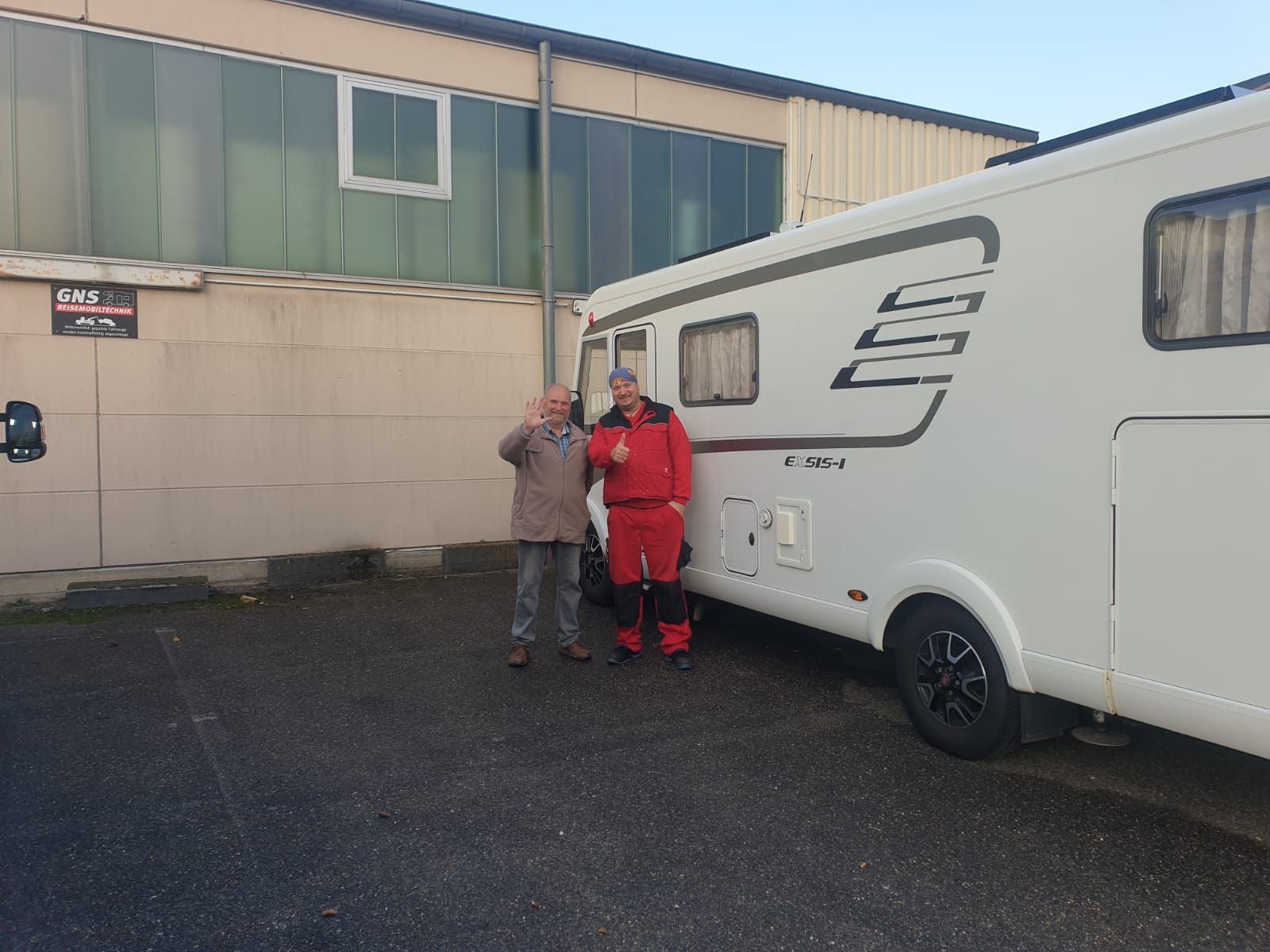 Zwei Männer stehen auf einem Parkplatz neben einem weißen Wohnmobil.