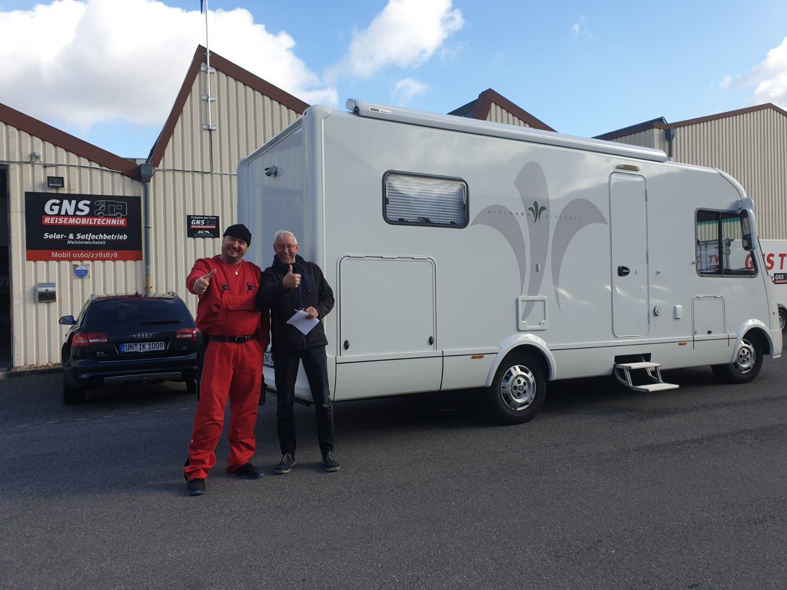 Zwei Männer stehen vor einem großen weißen Wohnmobil.