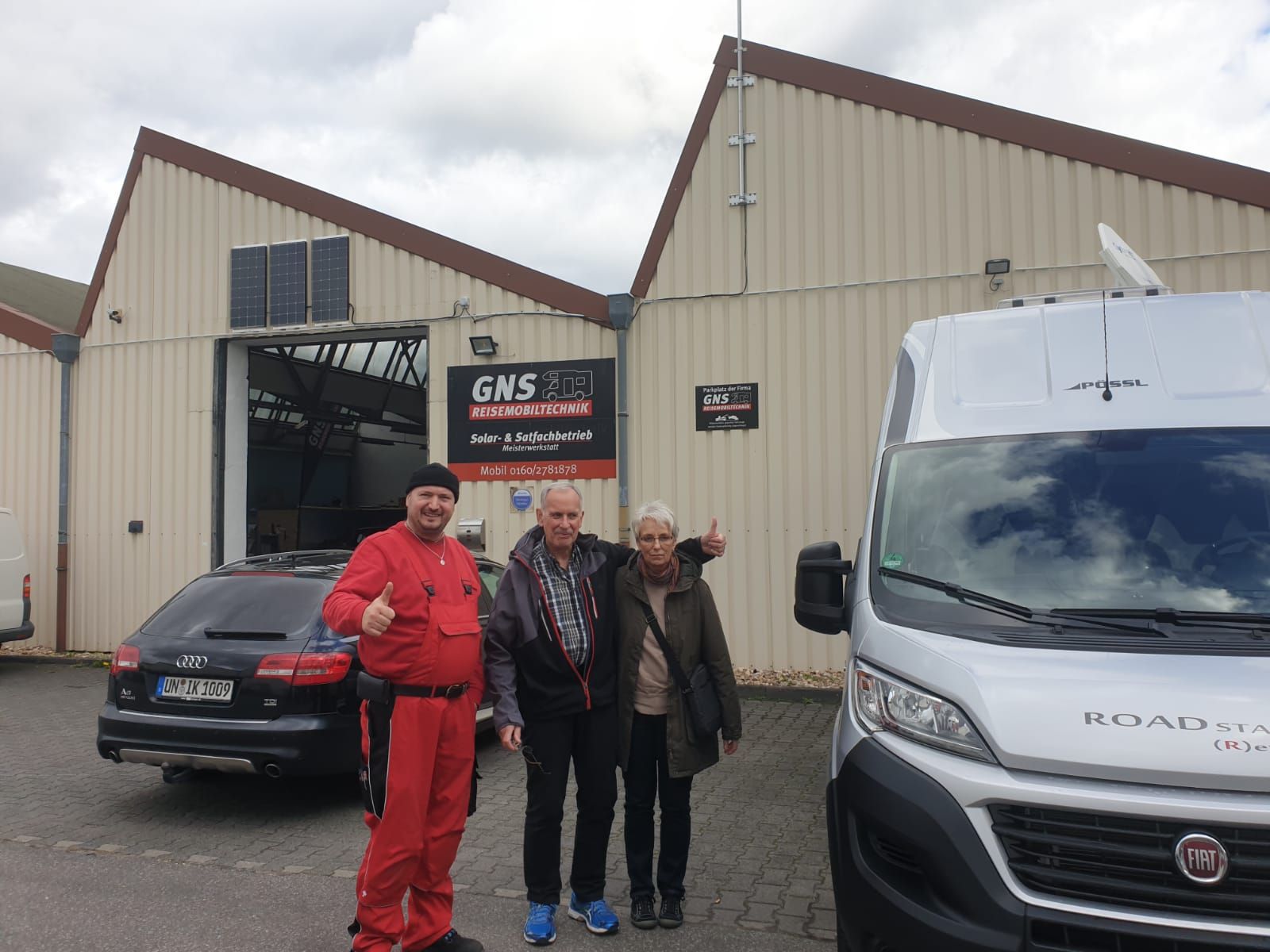 Eine Gruppe von Menschen steht vor einem Gebäude und einem Lieferwagen.