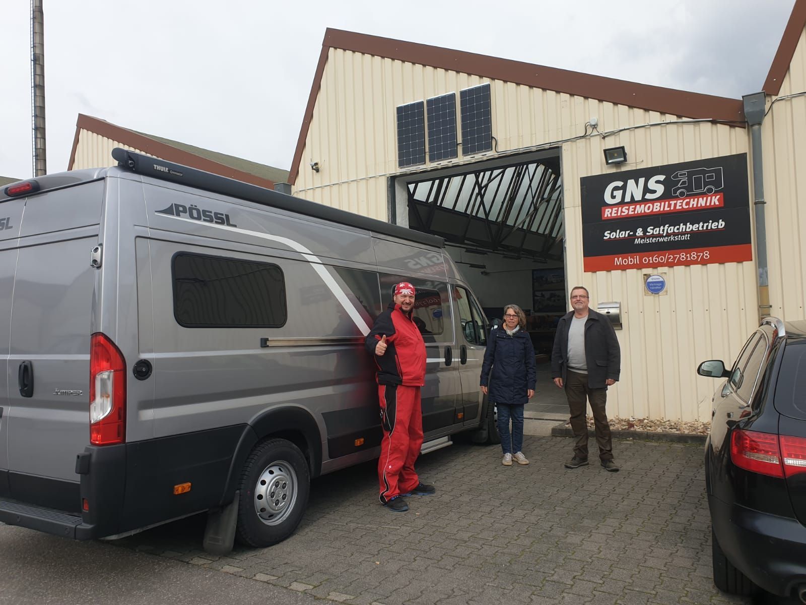 Eine Gruppe von Menschen steht neben einem Lieferwagen vor einem Gebäude.