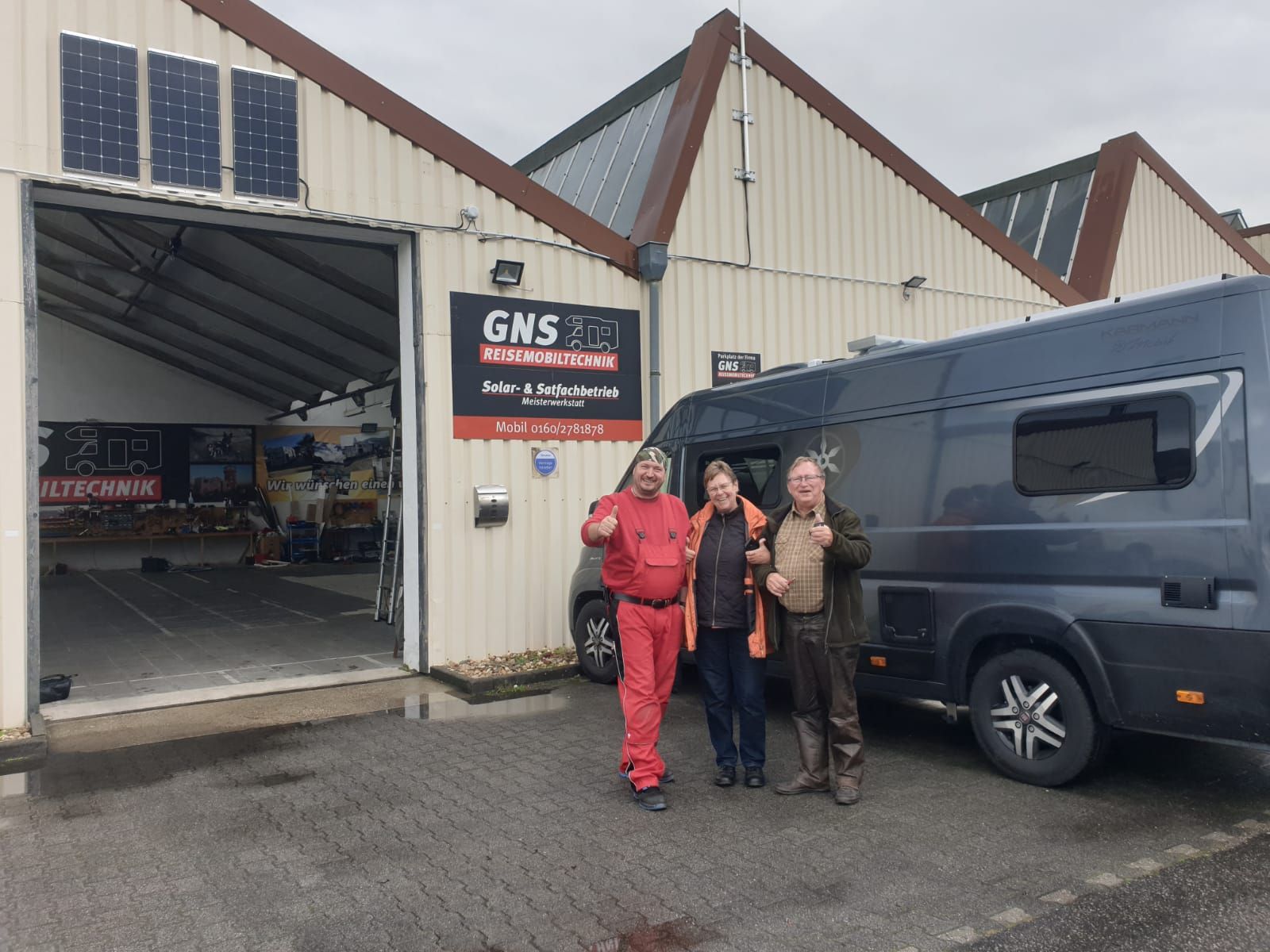 Eine Gruppe von Menschen steht vor einem Gebäude, vor dem ein Lieferwagen geparkt ist.