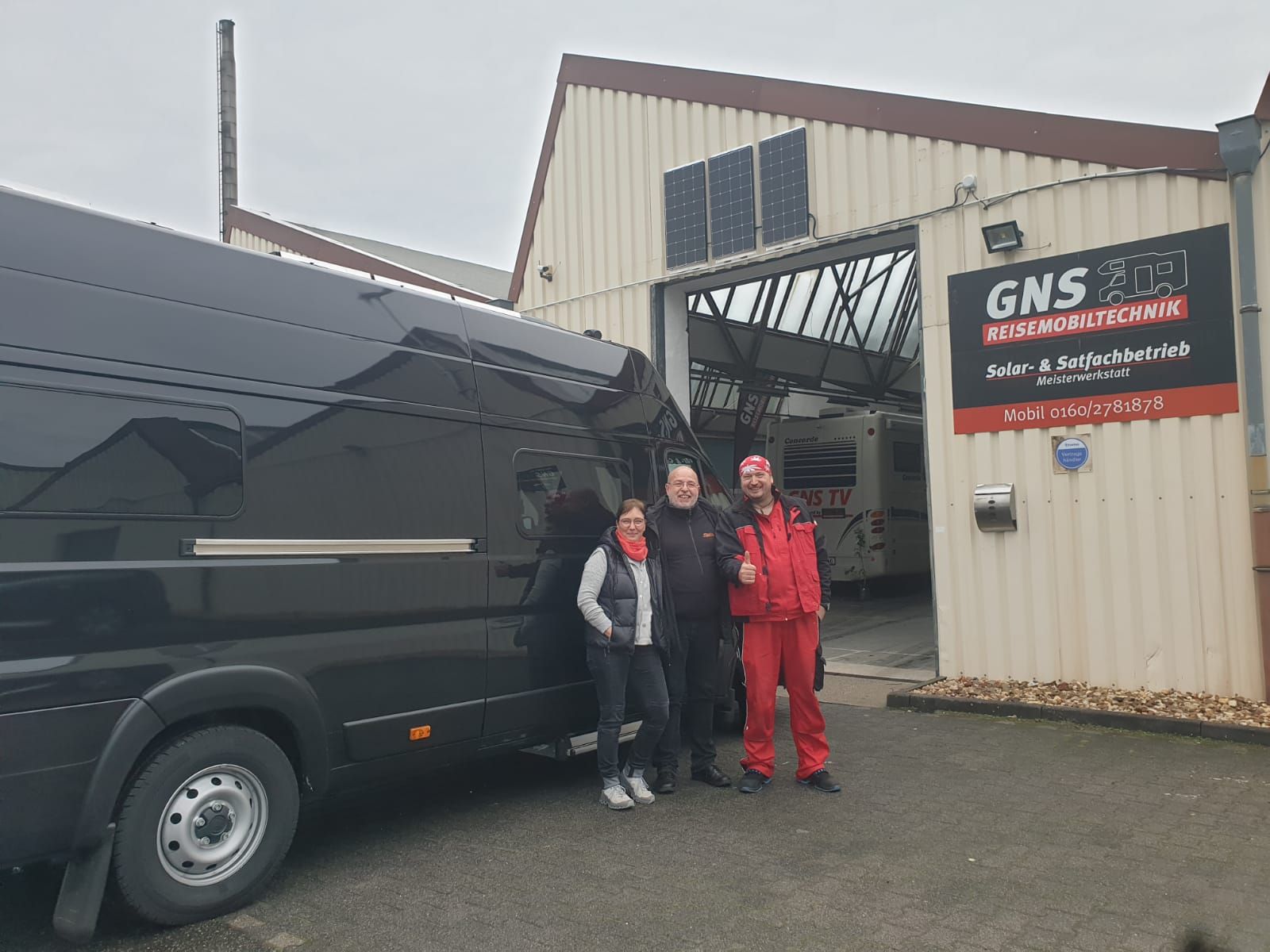 Eine Gruppe von Menschen steht vor einem schwarzen Lieferwagen.