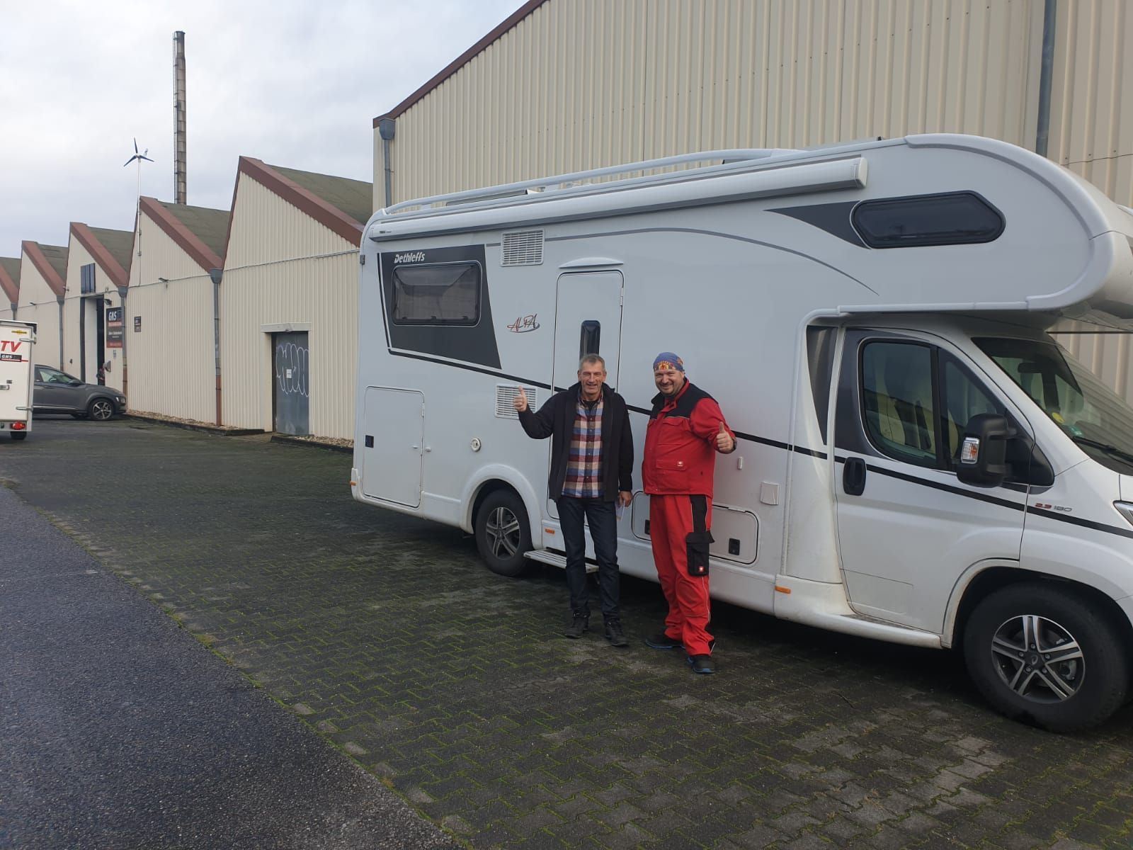 Zwei Männer stehen auf einem Parkplatz neben einem weißen Wohnmobil.