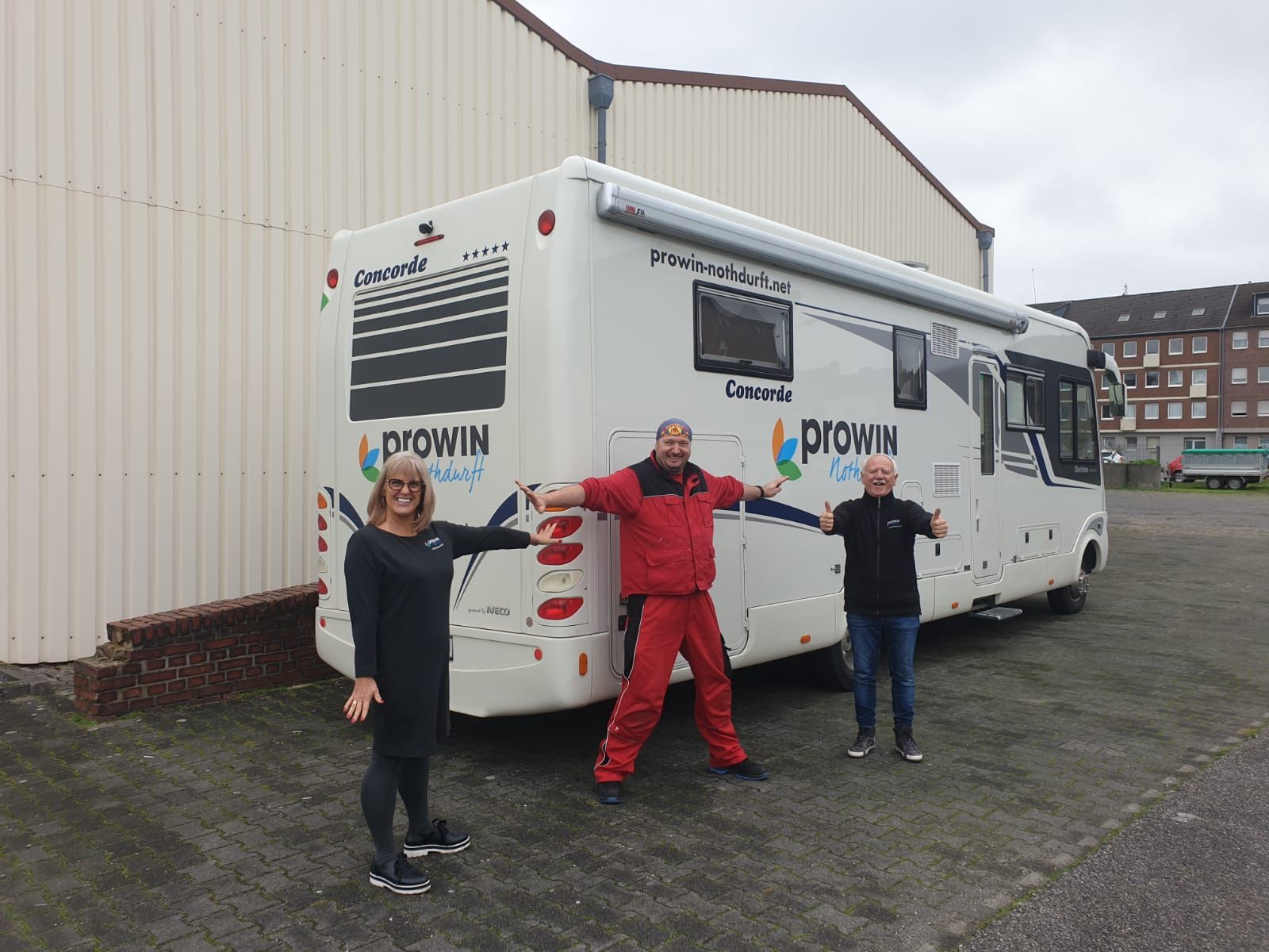 Drei Personen stehen vor einem großen weißen Wohnmobil.