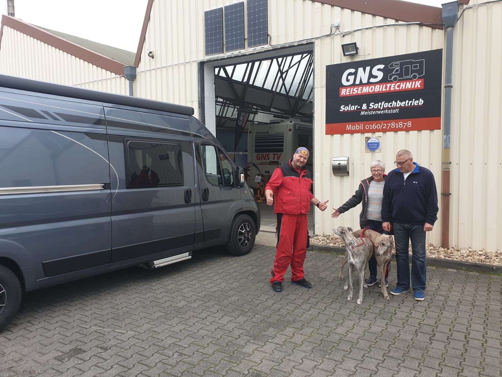 Drei Männer und zwei Hunde stehen auf einem Parkplatz vor einem Lieferwagen.