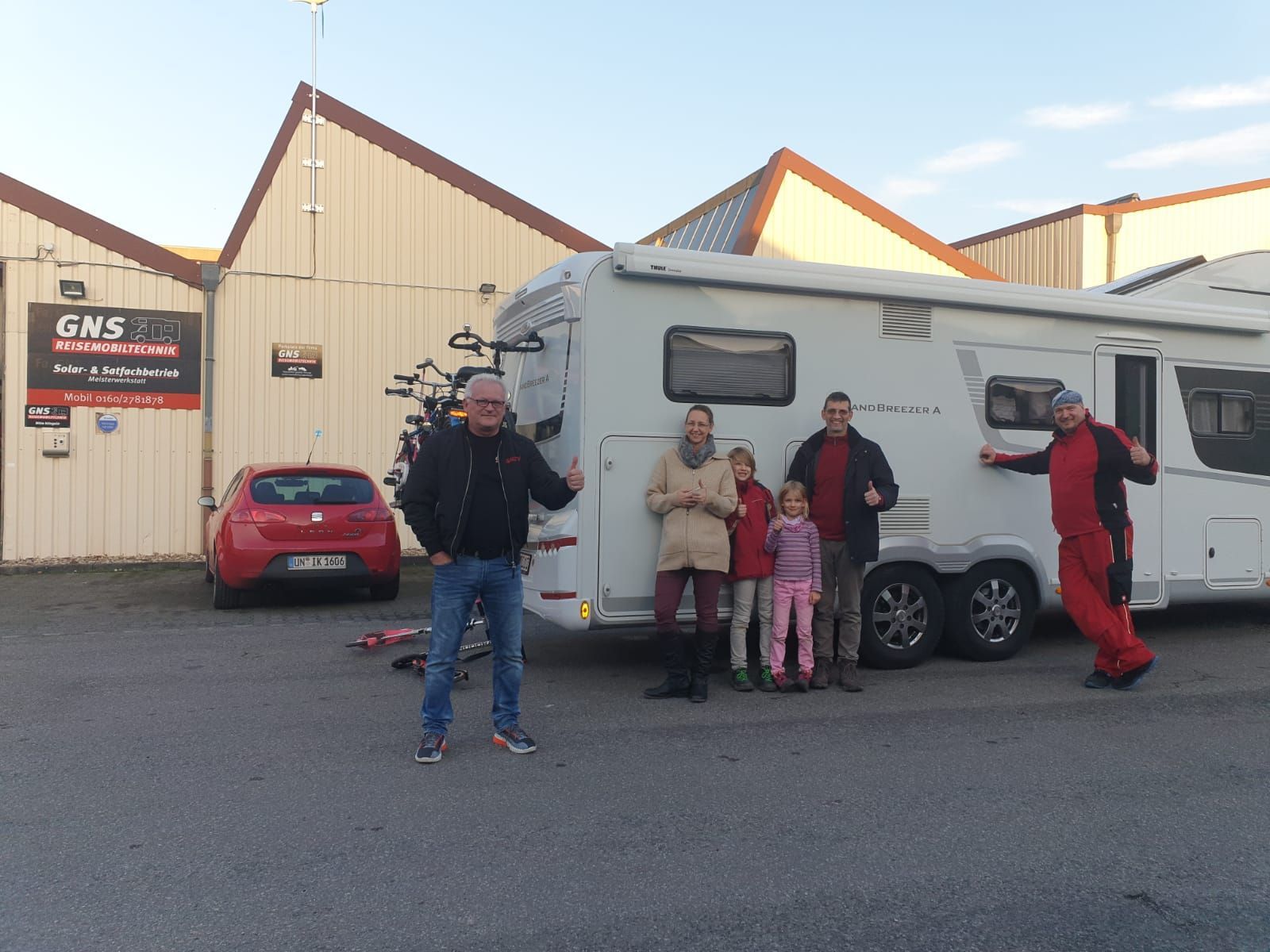 Eine Gruppe von Leuten steht auf einem Parkplatz vor einem Wohnmobil.