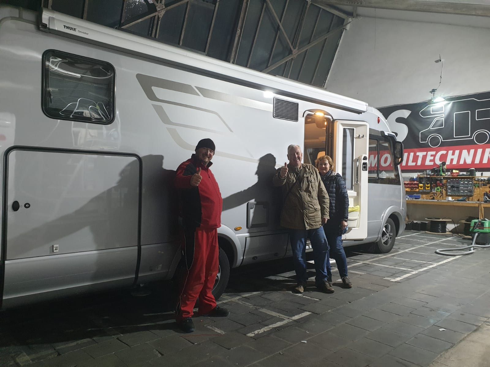 Drei Männer stehen auf einem Parkplatz vor einem Wohnmobil.