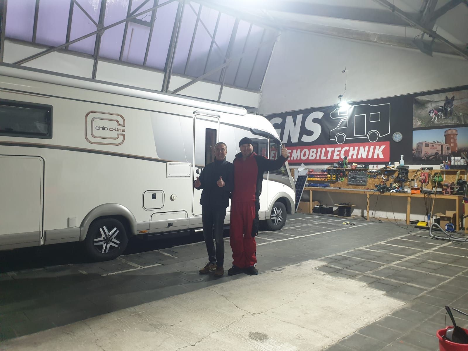 Zwei Männer stehen vor einem Wohnmobil in einer Garage.