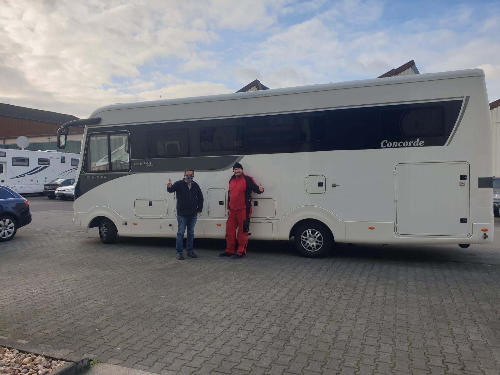 Zwei Männer stehen auf einem Parkplatz vor einem großen Wohnmobil.