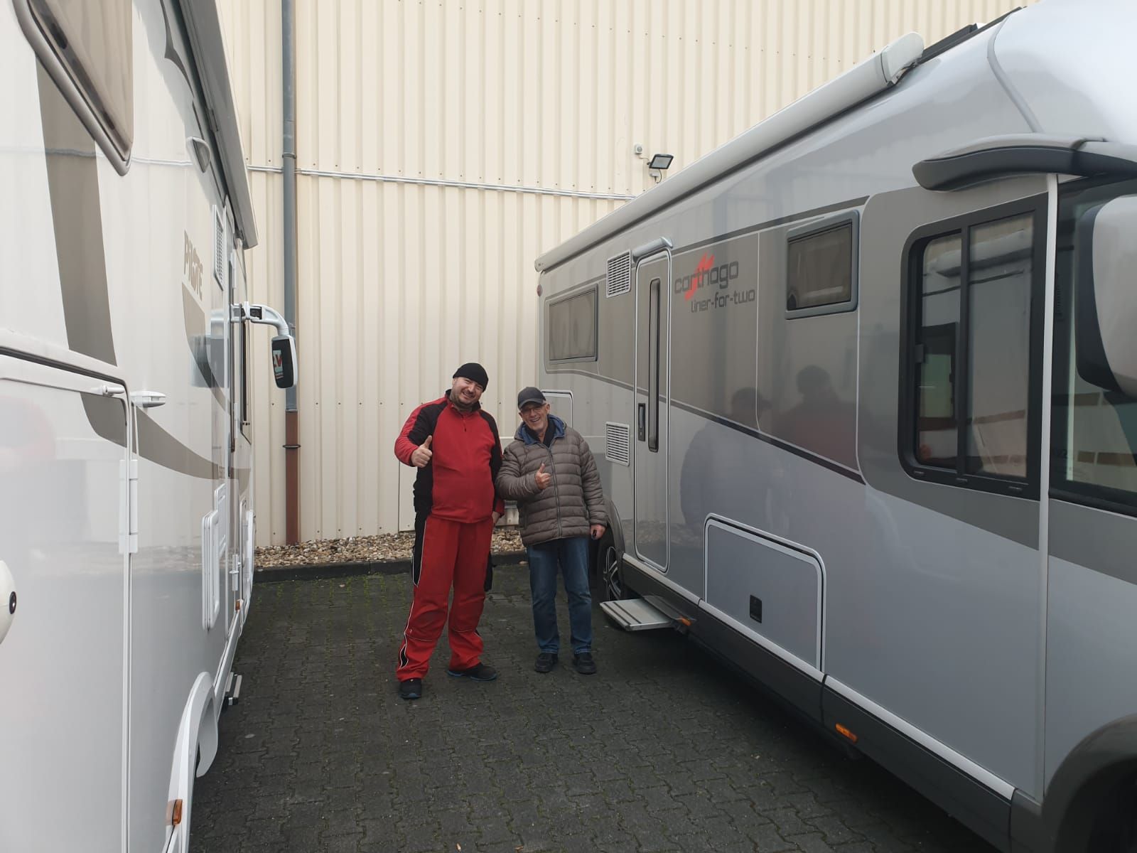 Zwei Männer stehen auf einem Parkplatz neben einem großen Wohnmobil.